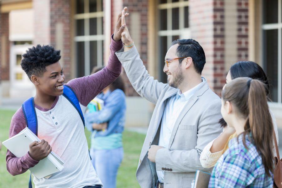 A principal high fives a high school student outside the school building